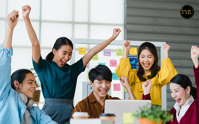 Happy team celebrating success around a laptop in the office